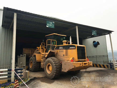 挖掘机正将建筑废料投放到投料口。